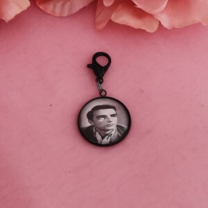 Op de afbeelding: Zwarte metalen hanger met een ronde glazen foto-inzet met een zwart-witfoto van een man.
