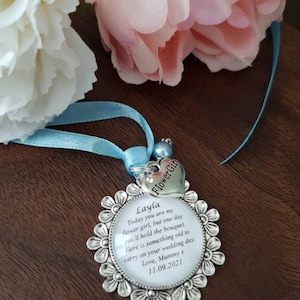 K&ouml;nnte beinhalten: Ein silberner Anh&auml;nger mit wei&szlig;em Hintergrund und schwarzem Text, der lautet: "Layla Heute bist du meine Blumenm&auml;dchen, aber eines Tages wirst du den Strau&szlig; halten. Hier ist etwas Altes, das du an deinem Hochzeitstag tragen kannst. Liebe, Mama x 11.09.2021". Der Anh&auml;nger ist an einem blauen Band und einem silbernen Herzanh&auml;nger befestigt, auf dem "Blumenm&auml;dchen" steht.