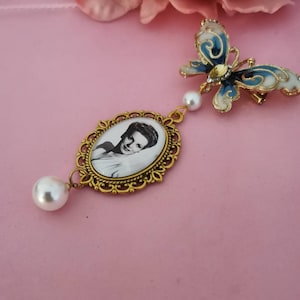 Un hermoso dije dorado para ramo con foto. Un recuerdo con forma de mariposa y diamantes de imitación, o un detalle azul para una novia el día de su boda.