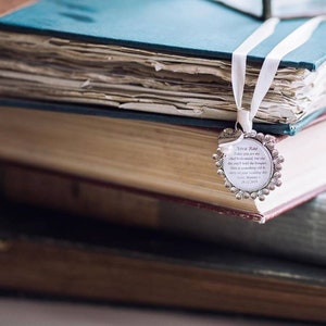 K&ouml;nnte beinhalten: Ein silbernes Lesezeichen mit floralem Design und einer personalisierten Botschaft f&uuml;r eine Brautjungfer. Das Lesezeichen h&auml;ngt an einem Stapel alter B&uuml;cher.