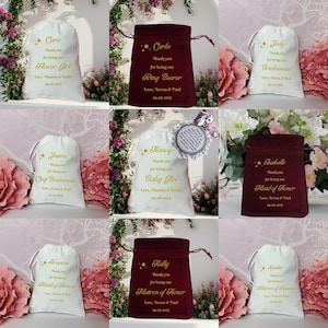 K&ouml;nnte beinhalten: Neun wei&szlig;e und burgunderfarbene Satin-Zugbeutel mit goldener Beschriftung. Jeder Beutel hat einen anderen Titel, wie "Flower Girl", "Ring Bearer", "Chief Bridesmaid", "Baby Girl", "Maid of Honor" und "Matron of Honor".