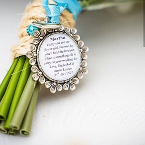 K&ouml;nnte beinhalten: Ein silberner Anh&auml;nger mit wei&szlig;em Hintergrund und schwarzem Text, der "Martha Today you are our flower girl, but one day you'll hold the bouquet. Here is something old to carry on your wedding day Love, Uncle Rob & Auntie Lauren 29th April 2021" lautet.