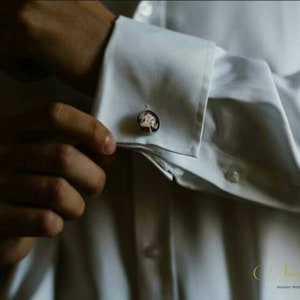 May include: A white dress shirt with a pair of cufflinks featuring a floral design.