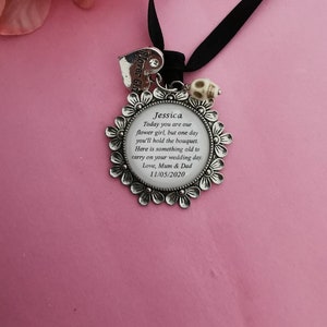 May include: Silver charm with a floral design and a white skull bead. The charm has a clear glass center with the text "Jessica Today you are our flower girl, but one day you'll hold the bouquet. Here is something old to carry on your wedding day. Love, Mum & Dad 11/05/2020".