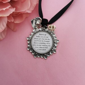 May include: A silver charm with a floral design and a message for a flower girl. The charm reads "Jessica Today you are our flower girl, but one day you'll hold the bouquet. Here is something old to carry on your wedding day. Love, Mum & Dad 11/05/2020".