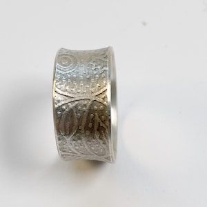 Könnte beinhalten: Ein silberner Ring mit einem strukturierten, gemusterten Design. Der Ring ist breit und hat eine abgerundete Form.