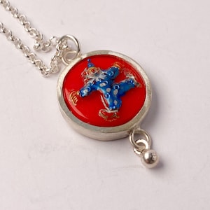 Op de afbeelding: Zilveren ketting met een rode en blauwe emaille hanger met een clownfiguur. De hanger is rond en heeft een zilveren lus.
