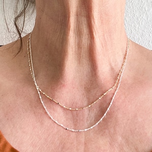 May include: A layered necklace with a silver chain and a gold chain. The chains are delicate and have a subtle sparkle.