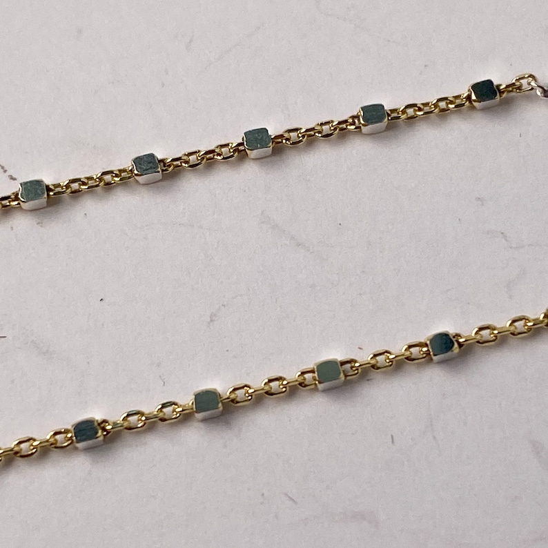 May include: A gold chain necklace with square-shaped links. The links are alternating gold and silver.