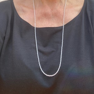 May include: A long, simple pearl necklace with small, white pearls. The necklace is worn by a person, but the person is not visible in the image.