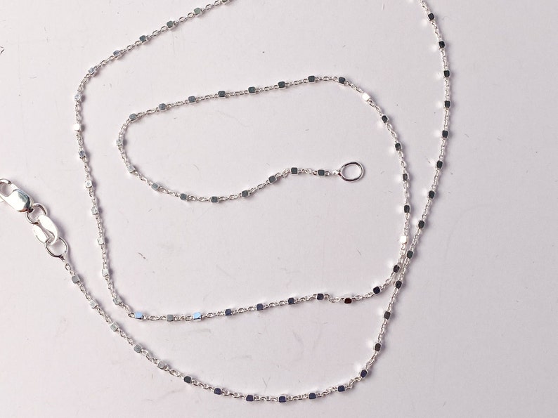 May include: A silver chain necklace with a square link pattern. The chain is about 18 inches long and has a lobster clasp.