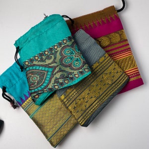 May include: Four small fabric pouches with drawstrings. The pouches are made of different colors and patterns, including turquoise, gray, brown, and pink. The pouches have gold and silver trim.