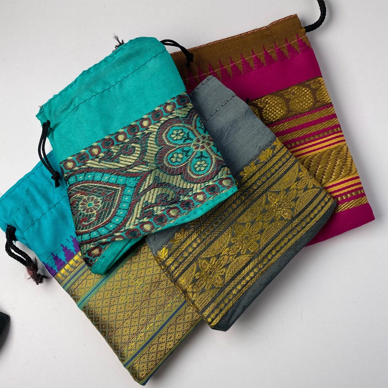 May include: Four small fabric pouches with drawstrings. The pouches are made of different colors and patterns, including turquoise, gray, brown, and pink. The pouches have gold and silver trim.
