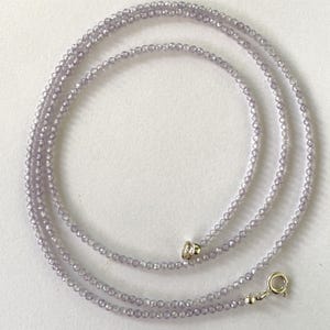 May include: A delicate lavender necklace composed of small, faceted beads. The necklace is strung together with a silver clasp and a small, decorative silver bead. The beads are evenly spaced, creating a subtle sparkle.