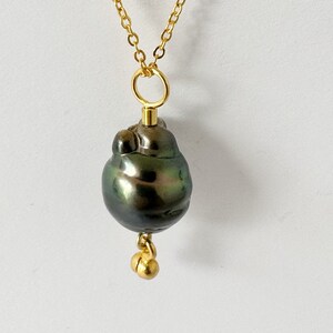 Può includere: Una collana con catena dorata con un ciondolo di grande perla barocca verde scuro. La perla ha una forma irregolare unica ed è accentuata da piccole perle dorate.