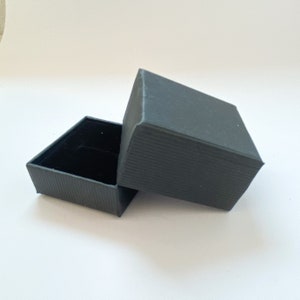 May include: A black, rectangular gift box with a textured lid. The lid is open and the box is empty.