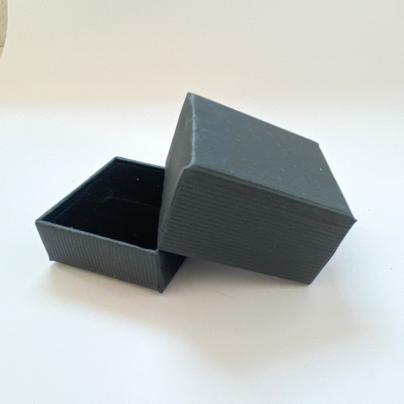 May include: A black, rectangular gift box with a textured lid. The lid is open and the box is empty.