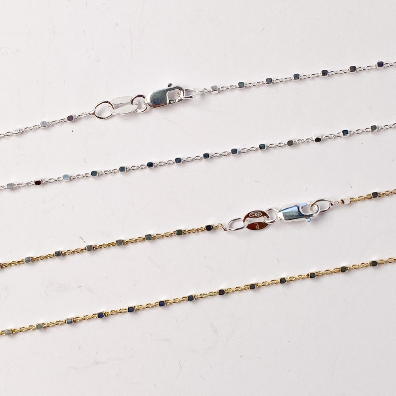 May include: Three silver chains with square links. The top two chains are silver and the bottom chain is gold.
