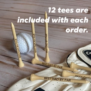 May include: A golf ball and wooden golf tees with the text "BEST DAD BY PAR". The image also includes a golf glove. The text "12 tees are included with each order" is also visible.