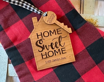 May include: A wooden home sweet home ornament with a keyhole design. The ornament is decorated with the text "Home Sweet Home" and the address "1055 Carolyn Ave.". A small round tag with the year "2022" is attached to the keyhole.