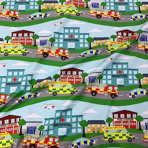 Può includere: Una stampa di tessuto colorata con un motivo ripetitivo di edifici cittadini, tra cui ospedali, caserme dei pompieri e stazioni di polizia. La stampa include anche vari veicoli di emergenza, come ambulanze, camion dei pompieri e auto della polizia. Lo sfondo è di colore azzurro chiaro con erba verde e nuvole bianche.