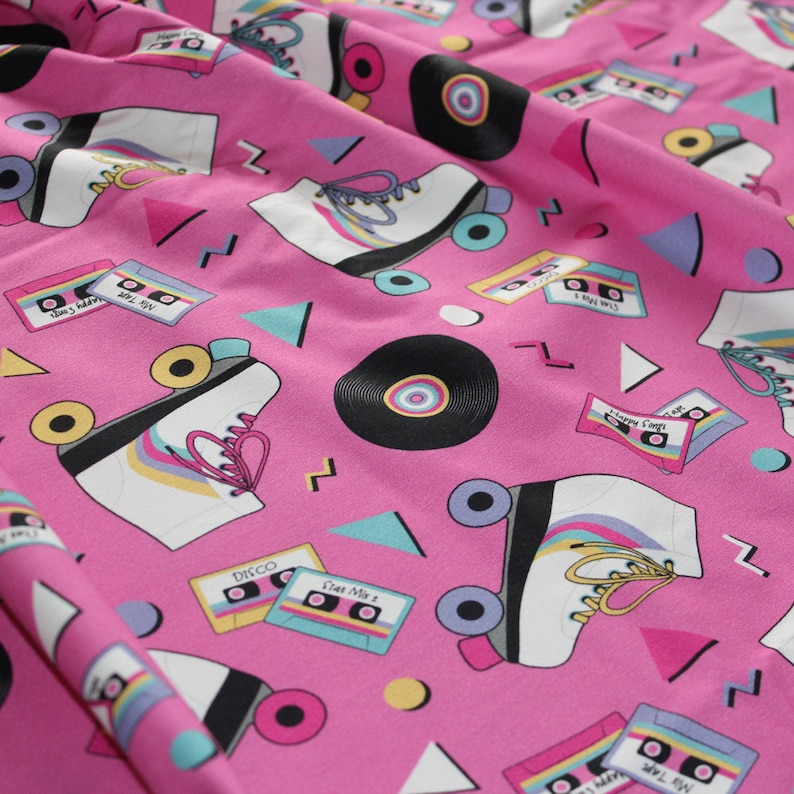 K&ouml;nnte beinhalten: Rosafarbener Stoff mit einem sich wiederholenden Muster aus Rollschuhen, Kassetten und Schallplatten. Die Rollschuhe sind wei&szlig; mit regenbogenfarbenen Rollen und Schn&uuml;rsenkeln. Die Kassetten haben verschiedene Titel, darunter "Star Mix 2", "Happy Camp" und "Mr. Jones's Album".