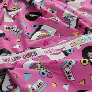 K&ouml;nnte beinhalten: Rosafarbener Stoff mit einem sich wiederholenden Muster aus Rollschuhen, Kassetten und Schallplatten. Der Stoff hat einen wei&szlig;en Rand mit dem Text "ROLLER DISCO" und "design by Becca Higgett SECOND".