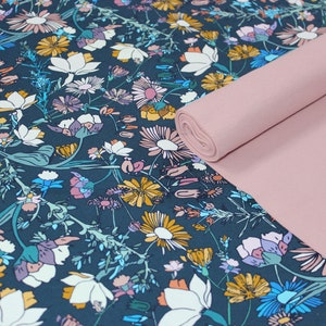 May include: A teal fabric with a floral pattern featuring various flowers in shades of pink, yellow, and blue. The fabric is rolled up and placed on top of a solid pink fabric.
