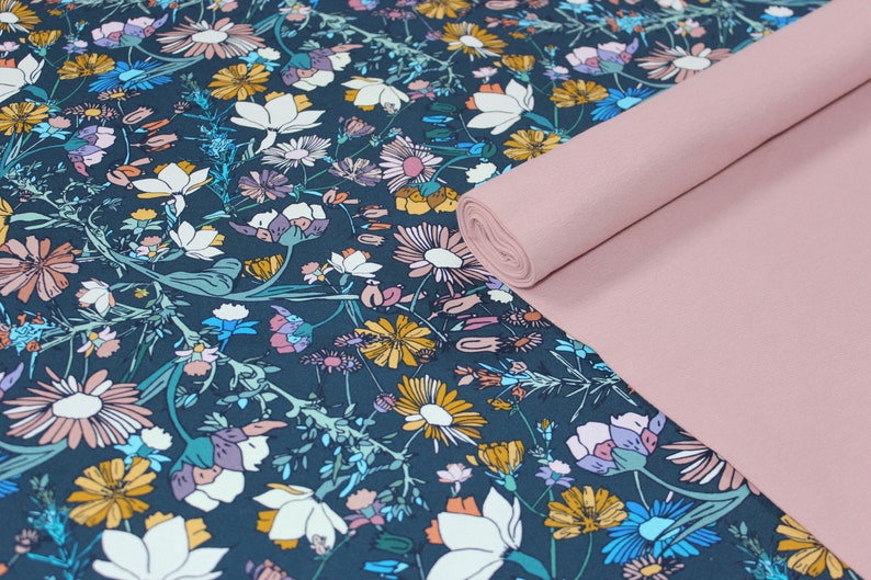 May include: A teal fabric with a floral pattern featuring various flowers in shades of pink, yellow, and blue. The fabric is rolled up and placed on top of a solid pink fabric.