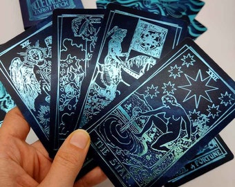 May include: A set of tarot cards with a blue and black color scheme. The cards feature illustrations of various figures and symbols, including a star, a figure holding a sword, and a figure riding a horse. The cards are part of the Blue Dreams Tarot Deck.