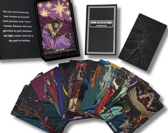 Può includere: Un mazzo di carte dei tarocchi in una scatola nera e dorata. Le carte presentano illustrazioni scure e dettagliate con un tema celeste. La scatola include un libro guida intitolato "Dark Reflections Guidebook".