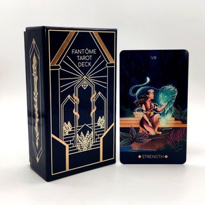 May include: A blue box with gold accents and the text "FANT&Ocirc;ME TAROT DECK" on the front.  Next to the box is a tarot card with the number "VIII" and the word "STRENGTH" on it. The card features a woman with a lion.