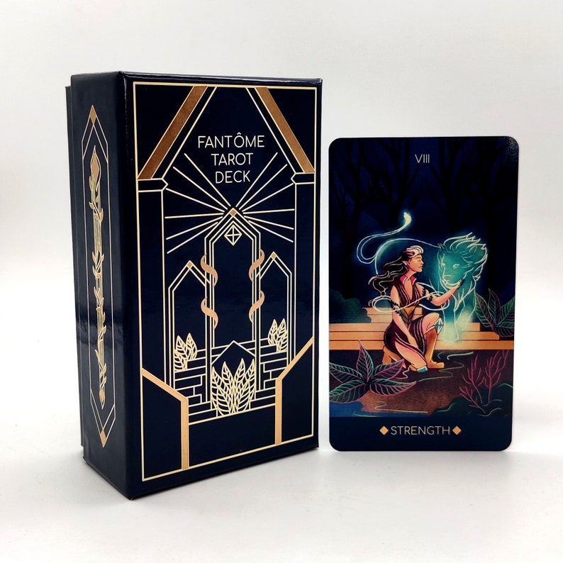 May include: A blue box with gold accents and the text "FANT&Ocirc;ME TAROT DECK" on the front.  Next to the box is a tarot card with the number "VIII" and the word "STRENGTH" on it. The card features a woman with a lion.