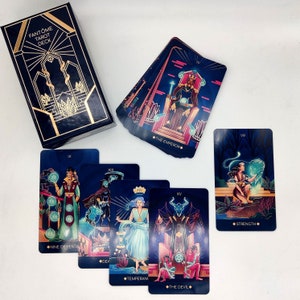 May include: A tarot deck with a dark blue and gold box. The cards feature illustrations of people and symbols in a dark blue, red, and gold color scheme. The cards include "The Emperor", "Strength", "Nine of Pentacles", "Temperance", and "The Devil".