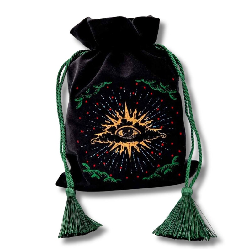 May include: Black velvet drawstring bag with a gold sunburst design featuring an eye, surrounded by red and white dots and green accents. The bag has green drawstrings and tassels.