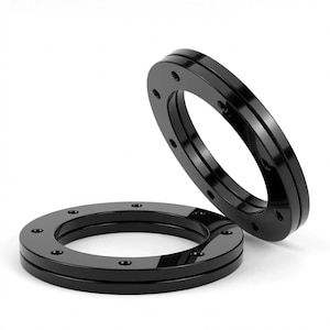 Könnte beinhalten: Zwei kreisförmige, glänzend schwarze Metallringe mit glatter Oberfläche. Jeder Ring weist eine Reihe von gleichmäßig verteilten, kleinen kreisförmigen Vertiefungen auf der flachen Oberseite auf. Ein Ring liegt flach, während der andere daran lehnt.