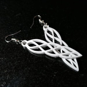 Könnte beinhalten: Ein Paar weiße Ohrhänger mit einem keltischen Knotendesign. Die Ohrringe sind aus leichtem Material gefertigt und haben einen silbernen Haken.