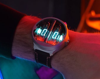 Könnte beinhalten: Eine silberne Uhr mit einem schwarzen Lederarmband und einem roten und grünen digitalen Display. Die Uhr wird am Handgelenk einer Person getragen.
