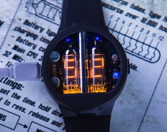 May include: A black wristwatch with a round face and a black band. The face of the watch is made of clear glass and shows the time using two orange glowing Nixie tubes. The watch is plugged into a charging cable.