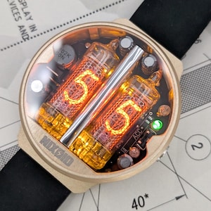May include: A Nixie tube wristwatch with a gold-toned circular case and a black silicone strap. The watch face displays the glowing orange number 55 through two vertical vacuum tubes. A small green LED indicator is visible on the right side.