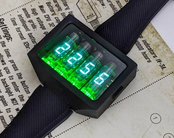 May include: A black wristwatch with a green digital display made of four Nixie tubes. The watch face displays the time "22:56". The watch is on a white surface with text about the watch's features.