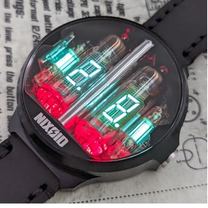 Può includere: Orologio Nixoid nero con quadrante rotondo che mostra numeri digitali in verde e rosso. L'orologio ha un cinturino in pelle nera e il testo "NIXOID" è visibile sul quadrante e sul lato. Il retro dell'orologio riporta la scritta "SPACE" e "MADE IN UKRAINE".