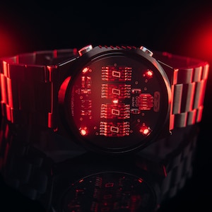 May include: A futuristic wristwatch with a black face and a metallic band. The watch face displays red illuminated digital components. The watch is set against a dark background with red lighting, creating a high-tech aesthetic.