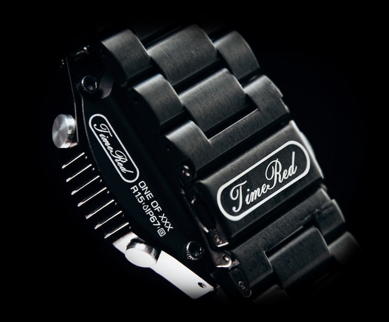 May include: Close-up of a black wristwatch with a metal band. The watch face and band feature the text "Time Red" in white script. The watch is marked "ONE OF XXX" and "R1.5.0IP67@".