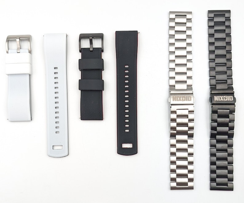 May include: Five different watch bands, including a white silicone band, a black silicone band, a black rubber band, a silver metal band, and a black metal band. The metal bands have the word "NIXON" engraved on the clasp.