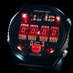 May include: Close-up of a black digital watch with a red illuminated display. The watch face shows the time in red digits, with an AM/PM indicator. The watch has a black band and a black background.