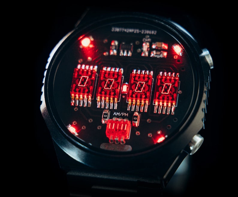 May include: Close-up of a black digital watch with a red illuminated display. The watch face shows the time in red digits, with an AM/PM indicator. The watch has a black band and a black background.