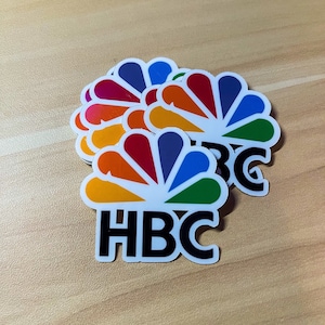 May include: A stack of colorful stickers featuring the NBC peacock logo and the letters "HBC" in black.