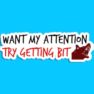May include: A white sticker with the text "WANT MY ATTENTION TRY GETTING BIT" in black and red, accompanied by a red illustration of a snarling wolf. The sticker is set against a bright blue background.