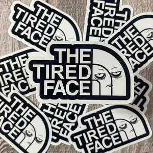 May include: Multiple white stickers with a black graphic of a tired face and the text "The Tired Face".